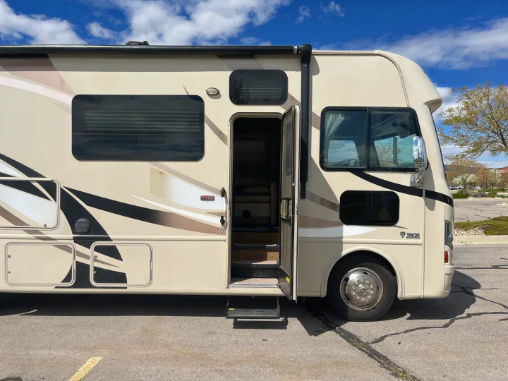 Beige RV rental parked with its entrance door open, showing steps inside, ready for a road trip adventure.. Thor A.C.E. 2016