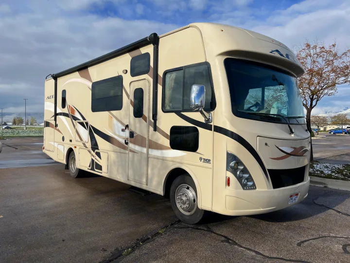 Cream-colored Thor Ace RV rental (motorhome) parked outdoors under a cloudy sky, with distant mountains.. Thor A.C.E. 2016