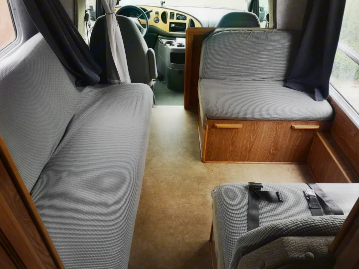 Inviting RV rental interior with comfy gray benches, wood accents, and a clear view to the front cabin.. Ford F350 2003