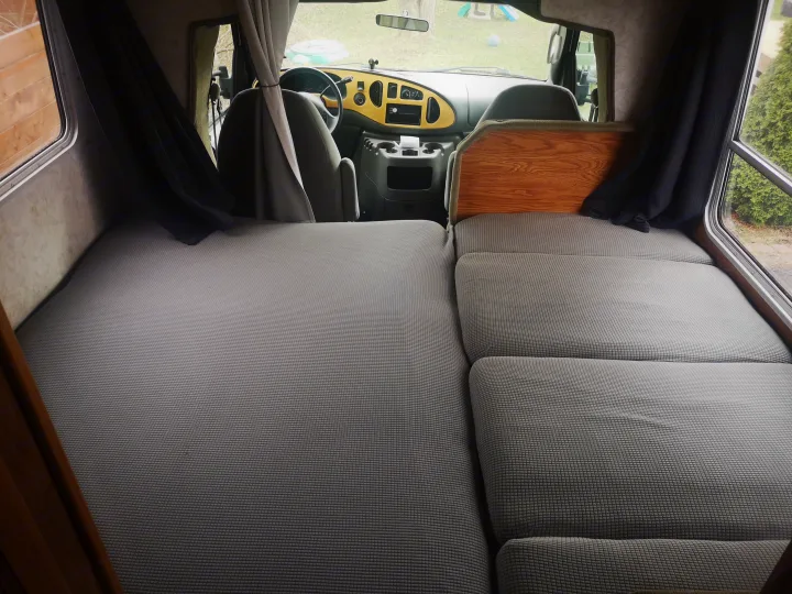 View inside an RV rental showing grey quilted bed/seating, dashboard, and side windows.. Ford F350 2003