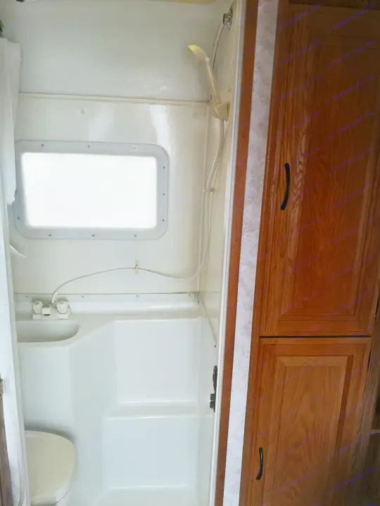 A compact, all-in-one bathroom within an RV rental, complete with a small shower, sink, toilet, and window.. Ford F350 2003