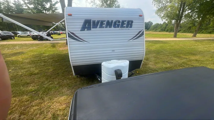 RV rental: A white Avenger travel trailer with extended awning, hitched, parked in a grassy camp area with vehicles.. Forest River Wildwood X-Lite 2023