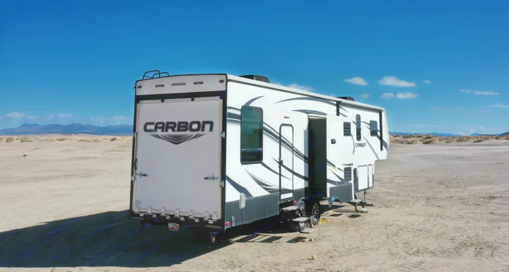 RV rental: A Carbon toy hauler with its ramp and side door open is parked in a vast desert landscape for camping.. Keystone RV Carbon Toy Hauler 2015