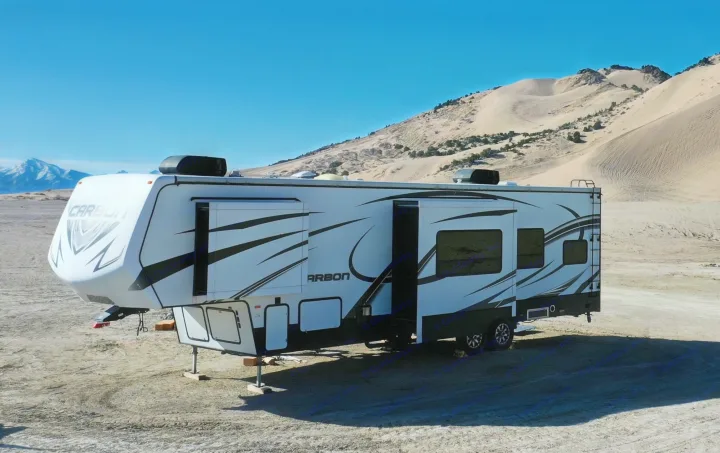Spacious RV rental parked at sandy dunes with distant snow-capped mountains. Ideal for desert adventure.. Keystone RV Carbon Toy Hauler 2015