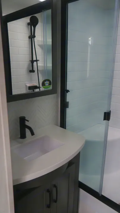 Modern RV rental bathroom: compact vanity, white sink, and glass shower with black fixtures.. Forest River Rockwood 2025