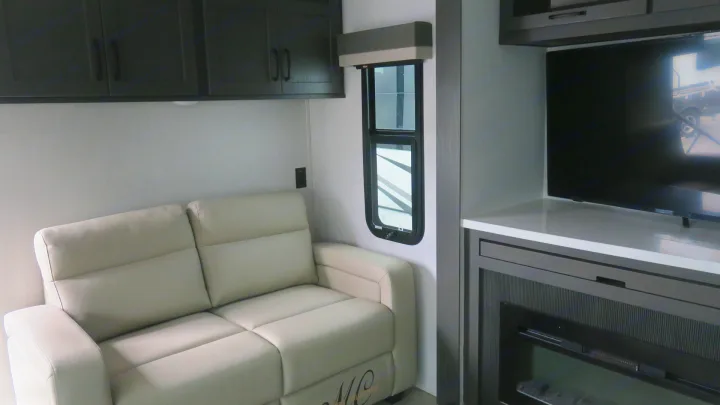 Cozy RV living area with a light sofa, dark cabinets, TV, and fireplace. Ideal for your next RV rental adventure.. Forest River Rockwood 2025