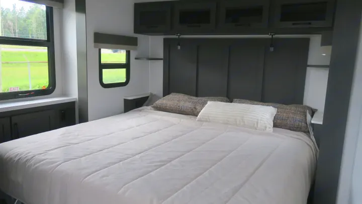 Spacious RV rental bedroom featuring a comfortable bed, dark gray headboard, overhead storage cabinets, and large windows with natural light.. Forest River Rockwood 2025