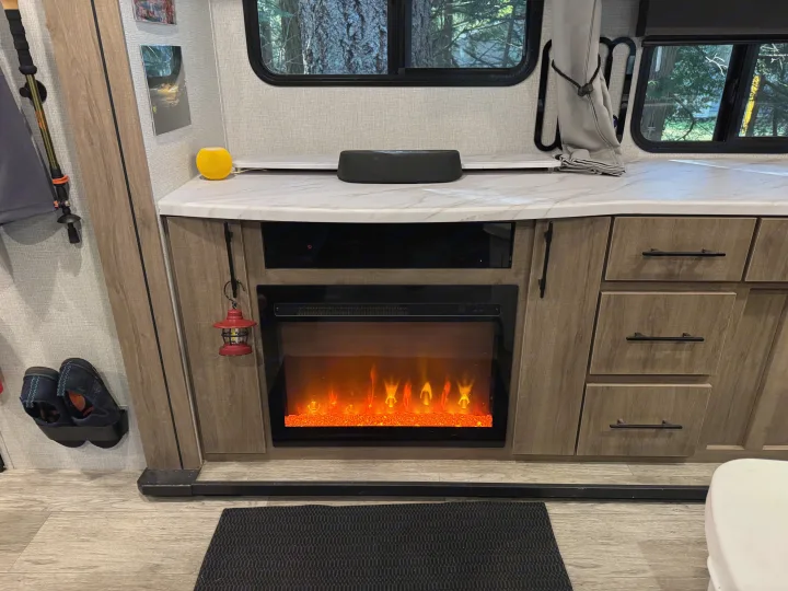 RV rental's inviting interior: electric fireplace, smart speakers, and forest views. Perfect for relaxing trips.. Grand Design Imagine 2023