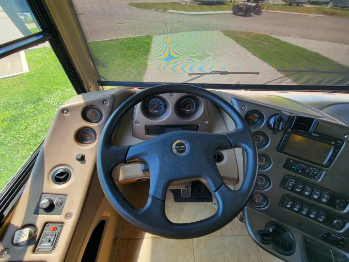 View from inside an RV rental. The cockpit features a steering wheel, dashboard, and gauges, with a screened view outside.. Forest River Berkshire 390-Bunkhouse 2012