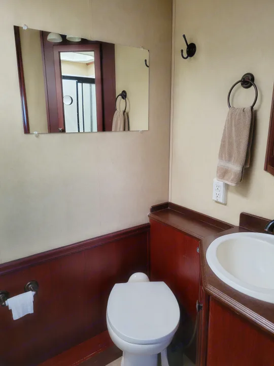 Compact RV rental bathroom features a white toilet, sink, mirror, and dark wood cabinetry.. Forest River Berkshire 390-Bunkhouse 2012