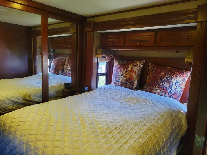 Comfortable RV rental bedroom featuring a quilted bed, patterned pillows, and rich wood cabinetry, with a mirrored closet.. Forest River Berkshire 390-Bunkhouse 2012