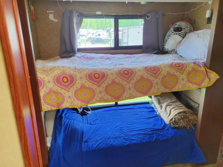 Cozy RV rental bunk beds with a colorful quilt and blue comforter. Window offers a view of the campsite.. Forest River Berkshire 390-Bunkhouse 2012