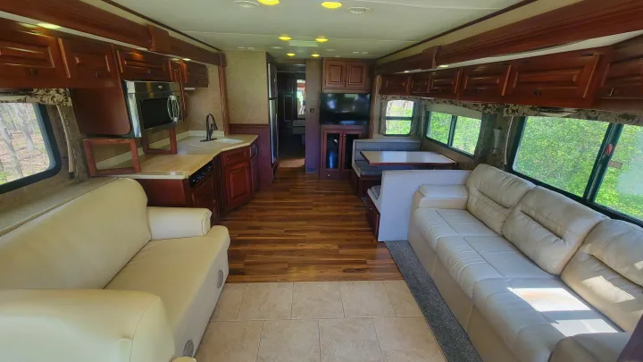 Expansive rv rental interior with cream-colored sofas, a well-equipped kitchen area, and a dining booth near windows.. Forest River Berkshire 390-Bunkhouse 2012