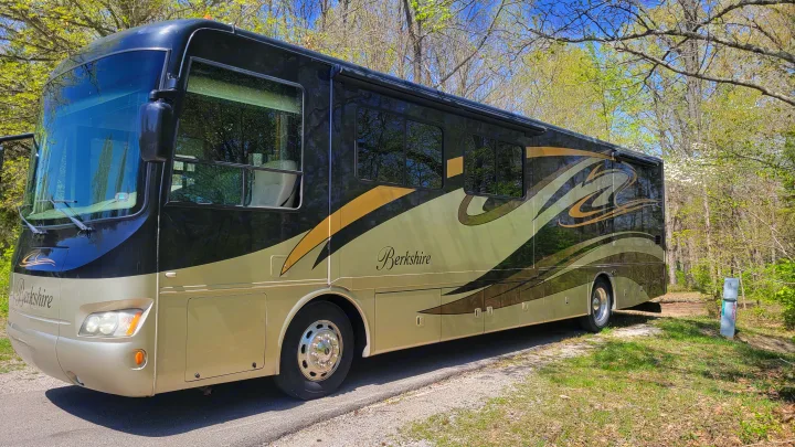 A black and gold Berkshire motorhome rv rental, parked at a lush campsite, ready for your next outdoor journey.. Forest River Berkshire 390-Bunkhouse 2012