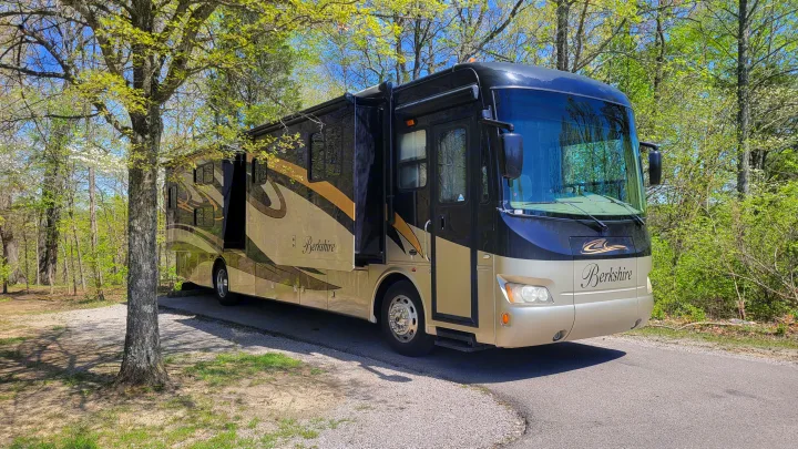 A large, black and tan Berkshire motorhome, perfect for rv rental, parked in a sunny, tree-filled campground.. Forest River Berkshire 390-Bunkhouse 2012