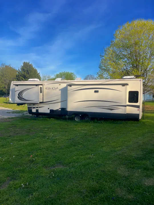 This Cedar Creek Champagne RV rental, a spacious travel trailer, is parked in a sunny green campsite under a blue sky.. Cedar Creek Champagne 2019