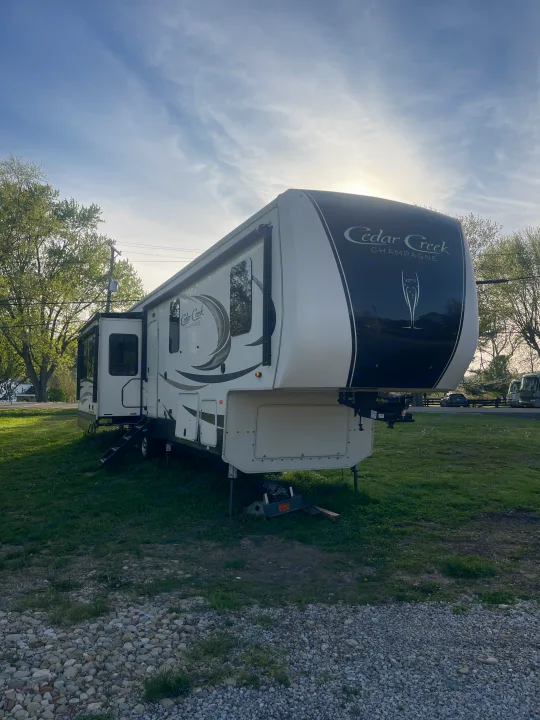 Cedar Creek Champagne fifth-wheel RV rental parked on green grass. This spacious travel trailer is ready for comfortable camping.. Cedar Creek Champagne 2019