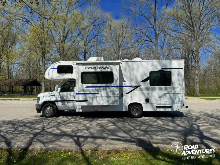 White Four Winds RV rental parked under sunny spring trees. Perfect for park adventures and exploring nature.. Thor Motor Coach Four Winds 2026
