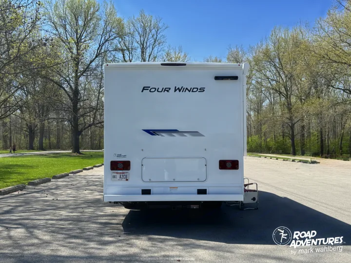 Back of a Four Winds RV rental, license plate 001 A2CU, parked in a sunny spring park with trees and grass.. Thor Motor Coach Four Winds 2026