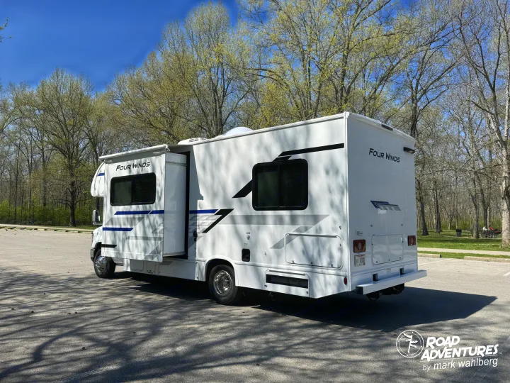 This white Four Winds RV rental, with its slide-out extended, is parked in a sunny, treed lot, ready for your road adventure.. Thor Motor Coach Four Winds 2026