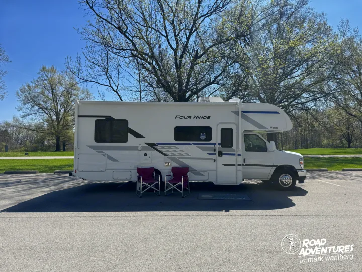 A white Four Winds RV rental, a Class C motorhome, parked with two chairs for road adventures under spring trees.. Thor Motor Coach Four Winds 2026