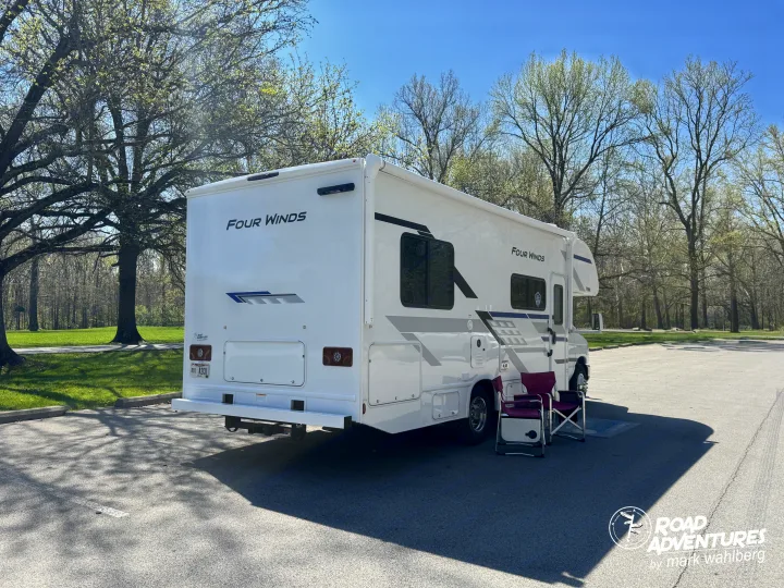 A white Four Winds RV rental motorhome is parked under spring trees with chairs, ready for a relaxing camping road trip.. Thor Motor Coach Four Winds 2026