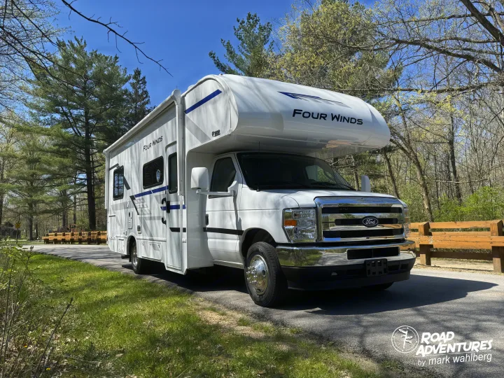 Explore nature with a Four Winds rv rental! White motorhome parked on asphalt by trees & benches in a scenic park setting.. Thor Motor Coach Four Winds 2026