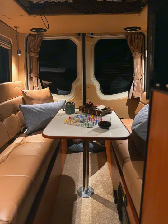 An inviting RV rental interior, showing a table set for a game, wine, and snacks between leather benches.. Sportsmobile Regular Body 2013
