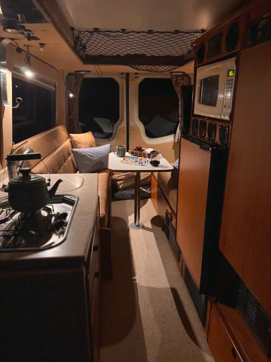 Cozy RV rental interior at night, featuring a dining area with a board game, snacks, and a kitchenette.. Sportsmobile Regular Body 2013