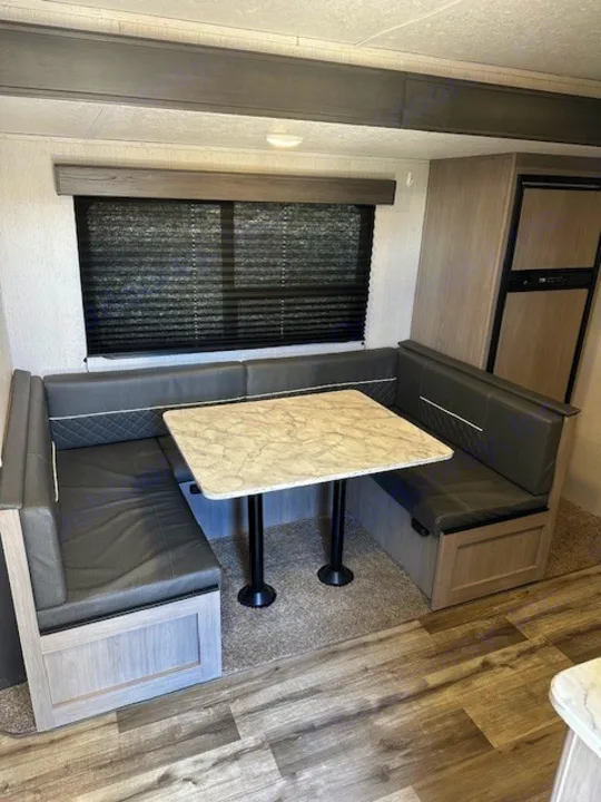 RV rental interior: Comfortable U-shaped dinette with grey upholstered benches, marble-look table, and large window.. Dutchmen Coleman Lantern 2022