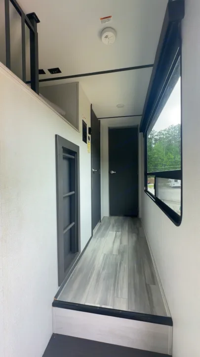 View inside an RV rental showing a step up to a hall with a loft, a large window, dark doors, and gray wood-look floor.. Keystone Sprinter 2022