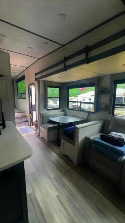 Explore this RV rental's cozy interior, featuring a dinette, sofa, and kitchen. Steps lead to a raised area for travel.. Keystone Sprinter 2022