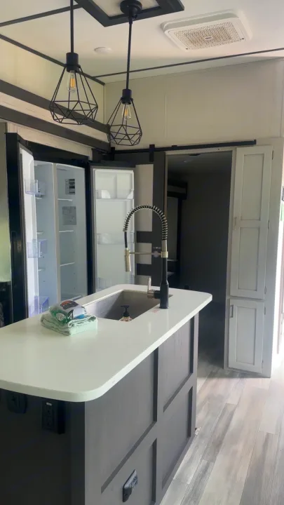 Modern RV rental kitchen island with sink, stylish pendant lights, and an open double-door refrigerator. Bright interior.. Keystone Sprinter 2022