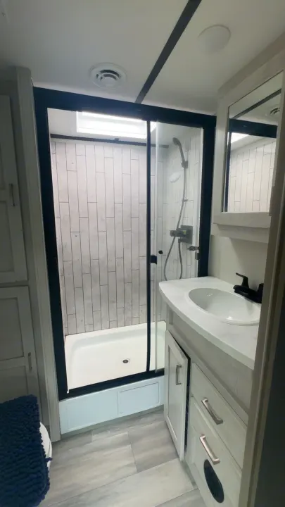 Bright, modern RV rental bathroom. Features a spacious glass shower, white vanity with sink, and light wood-look flooring.. Keystone Sprinter 2022