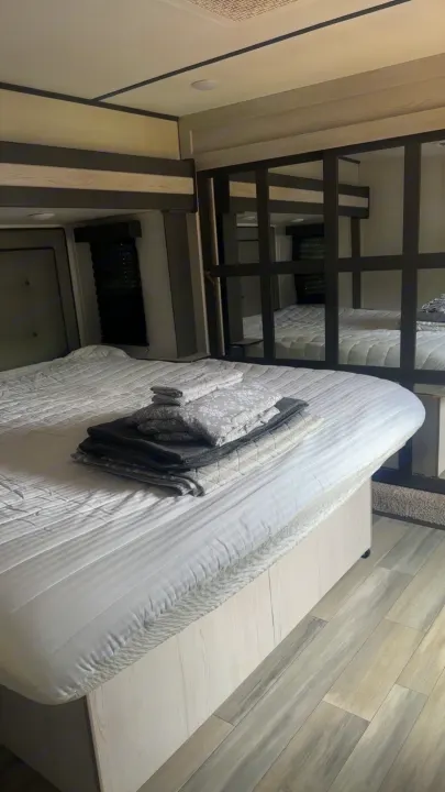 Spacious RV rental bedroom featuring a comfortable bed with fresh linens and modern mirrored accents.. Keystone Sprinter 2022