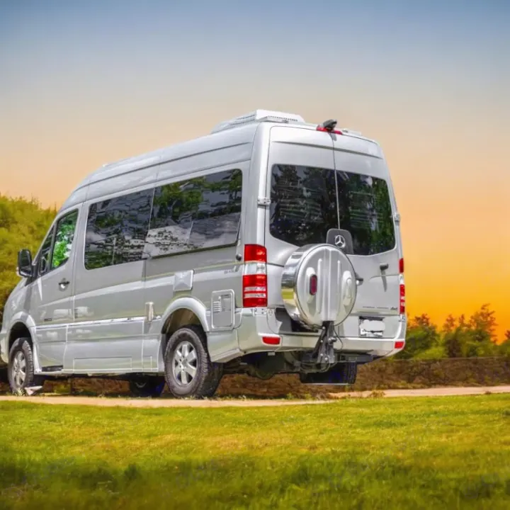 Rear view of a sleek silver rv rental camper van, parked on a dirt path beside green grass under a colorful sunset sky.. Roadtrek Roadtrek Class B 2017