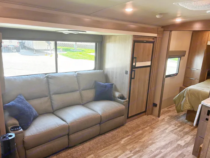 Inside a modern RV rental: comfortable living area with recliner sofa, refrigerator, and accessible private bedroom.. Grand Design Imagine 2022