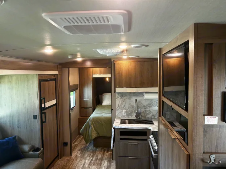 Inside a modern RV rental: a compact kitchen, comfortable bed, and living space with wood finishes.. Grand Design Imagine 2022