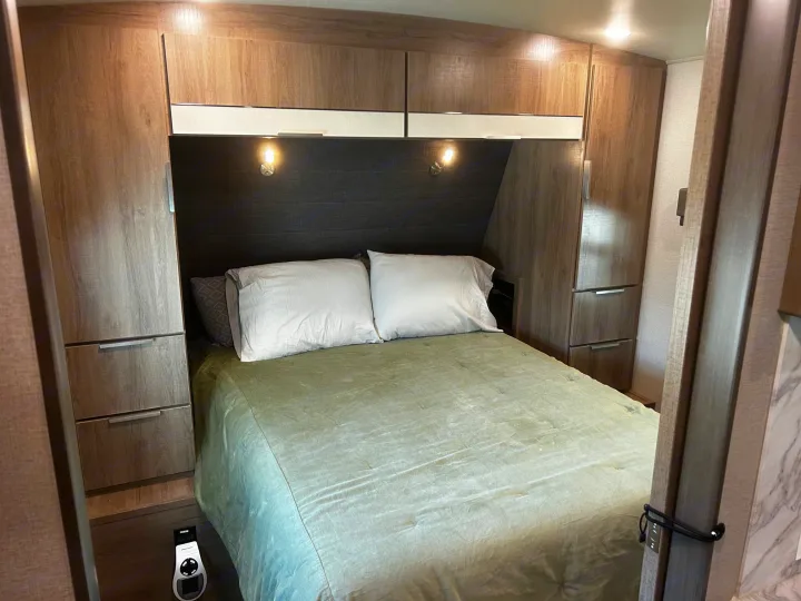 Cozy RV rental bedroom featuring a bed, white pillows, green comforter, and efficient built-in storage on both sides.. Grand Design Imagine 2022