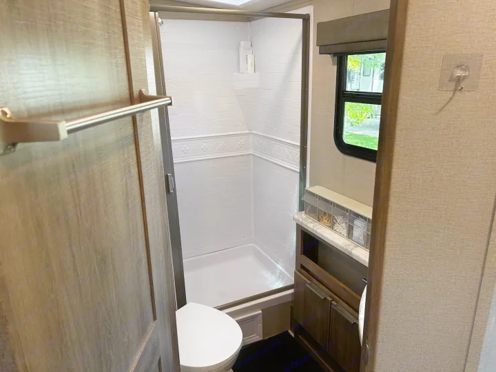 Compact RV rental bathroom features a clean shower, toilet, and vanity. Ideal for travelers seeking convenience on the road.. Grand Design Imagine 2022