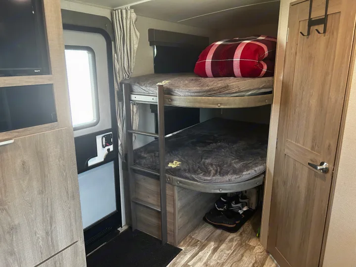 This RV rental interior features cozy bunk beds, a TV, and smart storage, perfect for camping trips.. Grand Design Imagine 2022