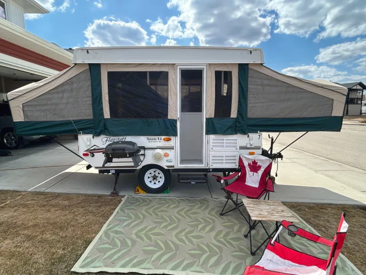 Pop-up RV rental set up for outdoor fun: patio rug, BBQ grill, and Canadian flag chairs provide comfort.. Forest River Flagstaff 2008