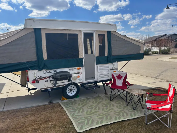 Enjoy an RV rental adventure! This pop-up camper setup features a BBQ, outdoor rug, and Canada-themed chairs.. Forest River Flagstaff 2008