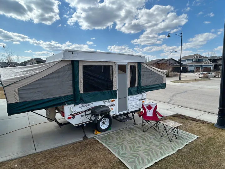 Enjoying the outdoors with an RV rental! A pop-up camper set up in a driveway with a grill, Canadian chair, and rug for comfort.. Forest River Flagstaff 2008