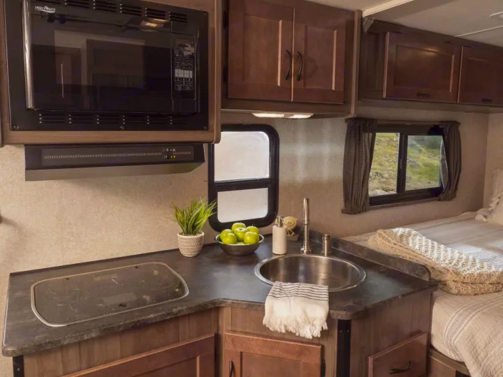 Explore this compact RV rental's interior: a well-equipped kitchen with microwave, sink, and stovetop, plus a comfortable bedroom.. Winnebago Minnie Winnie 2020