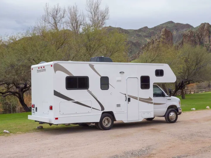 Adventure awaits! This white Minnie Winnie RV rental is parked on a scenic dirt path with mountains in the background.. Winnebago Minnie Winnie 2020