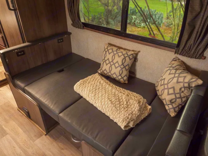 Relax in this RV rental's versatile seating area: comfy dark cushions, decorative pillows, a cozy blanket, and scenic window.. Winnebago Minnie Winnie 2020