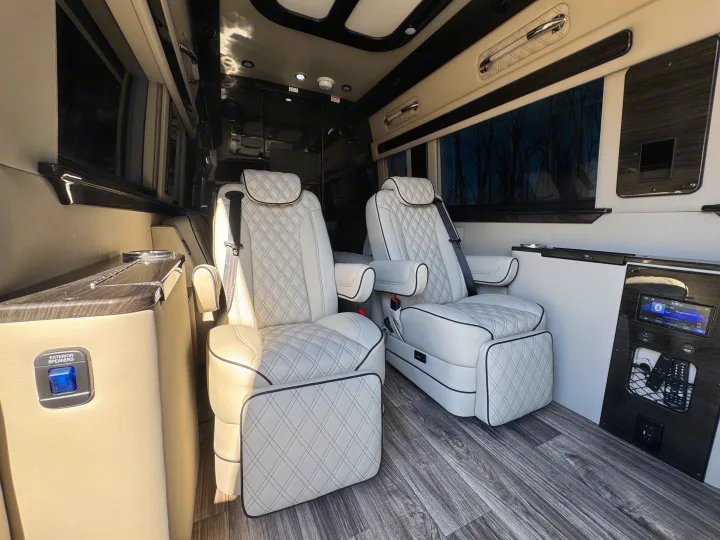 Luxury RV rental interior: plush white captain's chairs, wood floor, and tech controls for a premium travel experience.. Mercedes-Benz Sprinter 2026