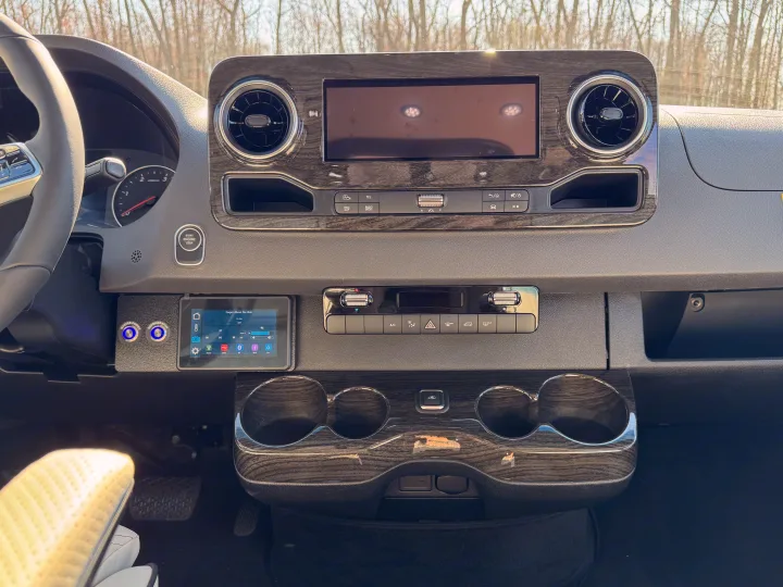 Detailed RV rental dashboard: steering wheel, infotainment screen, climate controls, custom power & refrigerator buttons.. Mercedes-Benz Sprinter 2026