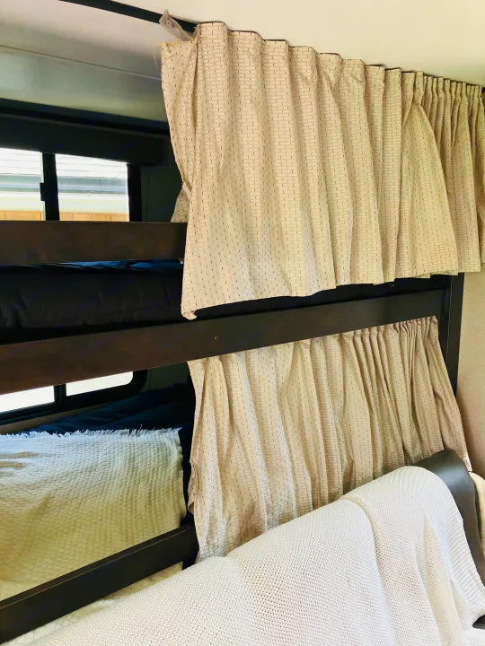 Inside an RV rental, showing two comfortable bunk beds with privacy curtains and cozy bedding.. Grand Design 265BH 2023